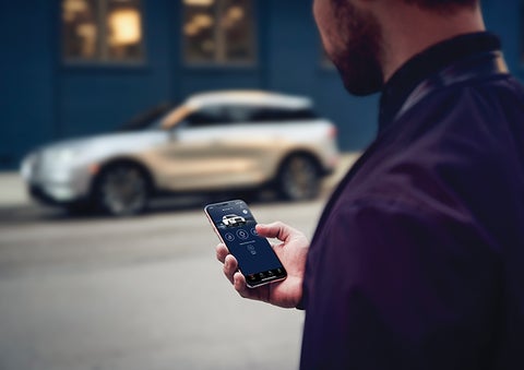 A person is shown interacting with a smartphone to connect to a Lincoln vehicle across the street. | Lincoln of Cutler Bay in Miami FL